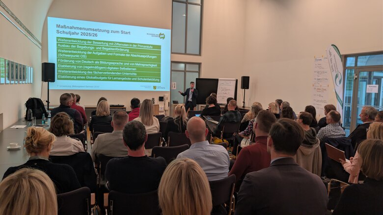 Ein Mann hält einen Vortrag vor einem Publikum. Seine Präsentation wird an die Wand projiziert.