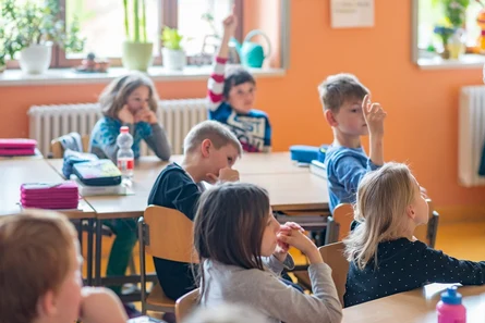 viele Kinder in einem Klassenraum sitzen an ihren Tischen auf Stühlen