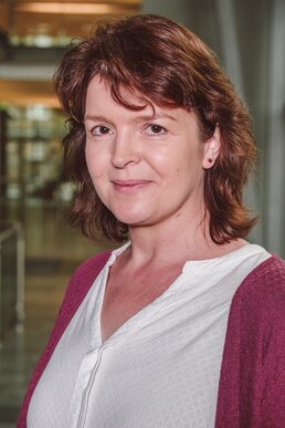 Portraitfoto von einer Frau mit einer weißen Bluse und roter Strickjacke.