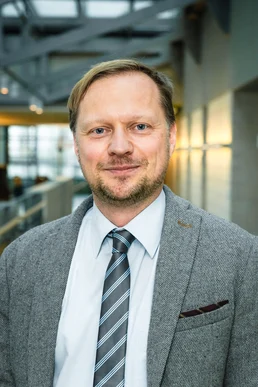 Portrait von einem Mann mit einem grauen Jackett, weißem Hemd und einer gestreiften Krawatte.