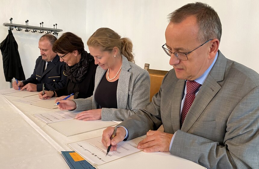 Unterzeichnung der Kooperationsvereinbarung von vier Personen sitzend an einem Tisch.