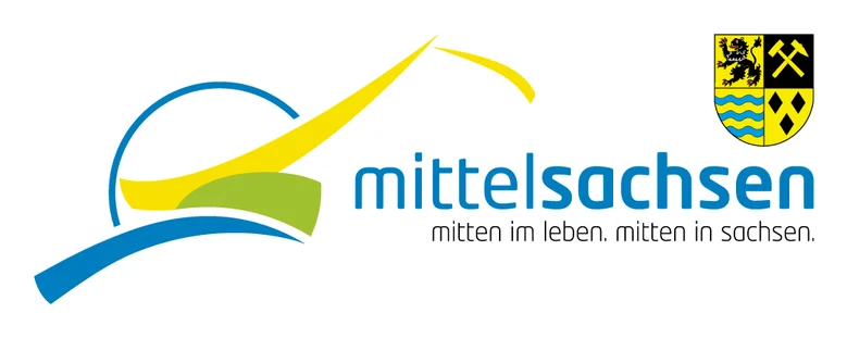 Auf der linken Seite des Logos sind mehrere blaue, gelbe und grüne Linien. Daneben steht "mittelsachsen" in blauer Schrift. Darunter steht in grau "mitten im leben. mitten in sachsen". Darüber, in der rechten oberen Ecke ist das Wappen des Landkreises, we