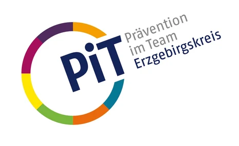 Links ist ein Kreis mit bunten Umrissen. An einer Stelle ist dieser unterbrochen und dort steht "PiT". Neben dem Kreis steht zudem "Prävention im Team" in grauer Schrift und darunter "Erzgebirgskreis" in blauer Schrift.
