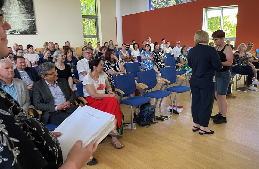 Mehrere Personen in einem Raum in Reihenbestuhlung schauen bei der Übergabe der Ergebnisse zu.