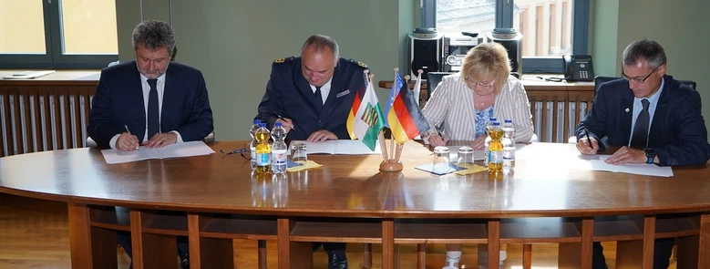 Vier Personen sitzen an einem Tisch und unterzeichnen die PiT-Kooperation.