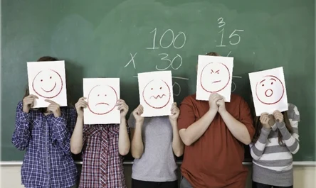 Fünf junge Personen stehen vor einer grünen Tafel und halten sich weiße Zettel vor die Gesichter. Darauf sind symbolhafte Gesichter gemalt, die verschiedene Gefühle ausdrucken.