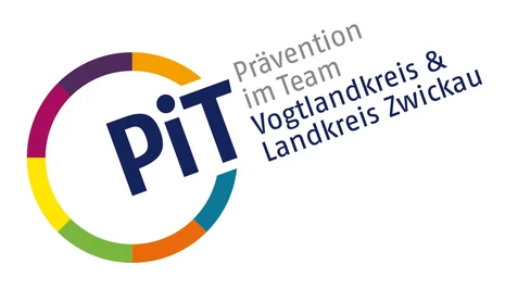 Links ist ein Kreis mit bunten Umrissen. An einer Stelle ist dieser unterbrochen und dort steht "PiT". Neben dem Kreis steht zudem "Prävention im Team" in grauer Schrift und darunter "Vogtlandkreis & Landkreis Zwickau" in blauer Schrift.