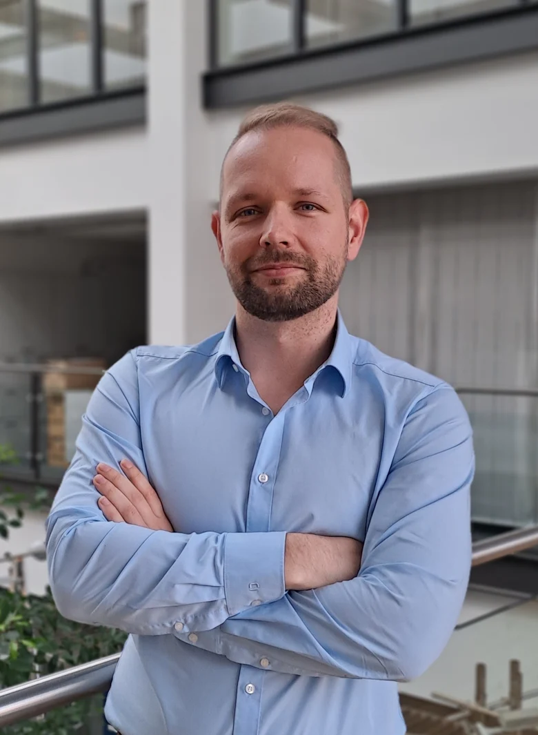 ein Mann steht mit verschränkten Armen und lächelt in die Kamera