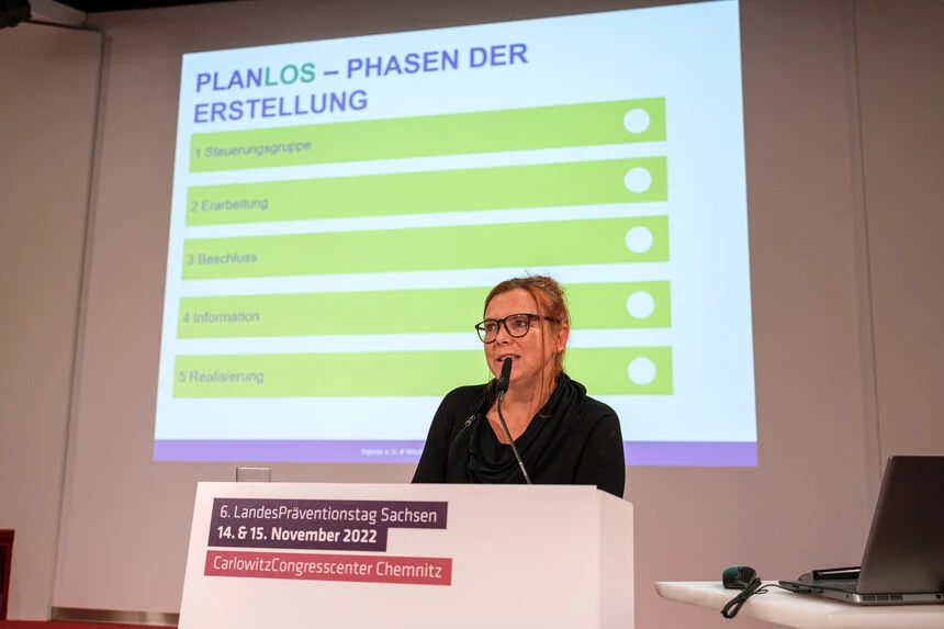 Eine Frau steht an einem Rednerpult und hält einen Vortrag. Hinter ihr ist eine Projektion der Präsentation zu sehen.