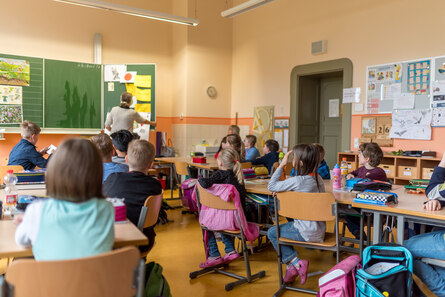 viele Kinder sitzen auf ihren Stühlen an ihren Tischen in einem Klassenraum