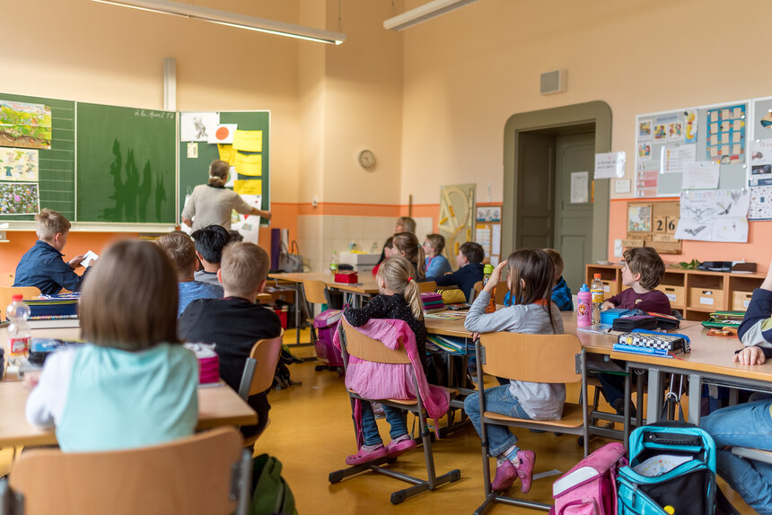 viele Kinder sitzen auf ihren Stühlen an ihren Tischen in einem Klassenraum